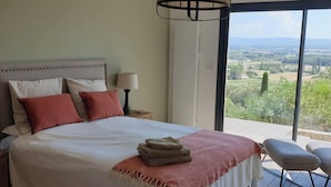 Un dormitorio con una cama grande, una mesita de noche, una lámpara y vistas al campo.