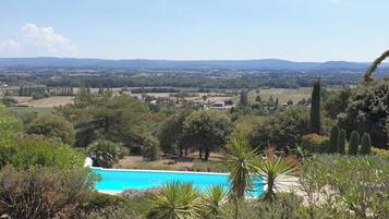 Une piscine entourée d’arbres, avec vue sur des champs et des collines lointains.
