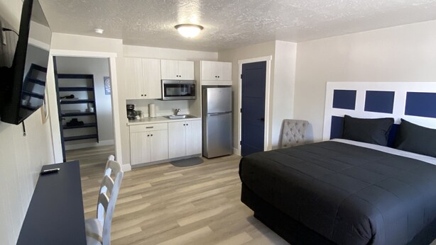 A modern bedroom with a large bed, a desk, and a kitchenette in the background. -  CB&M Duchesne Hotel (Duchesne)