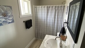 A bathroom with a white sink, a mirror, a shower curtain, and a window. -  CB&M Duchesne Hotel (Duchesne)
