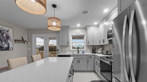 A modern kitchen with a large island, stainless steel appliances, and a view to the outside. - Outer Banks Haven: Pet-Friendly, Walk-to-Beach, EV Charging, Updated Kitchen (Kitty Hawk)