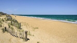 A sandy beach with a wooden fence and a pier in the background. - Outer Banks Haven: Pet-Friendly, Walk-to-Beach, EV Charging, Updated Kitchen (Kitty Hawk)