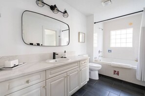Ein modernes Badezimmer mit einem weißen Waschtisch, einem großen Spiegel, einer Toilette und einer Badewanne.