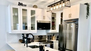 A modern kitchen with white cabinetry, a large island with stools, stainless steel appliances, and a black coffee maker. - Fairmont Oasis | Luxury | Views | Bright | Nature (Fairmont Hot Springs)
