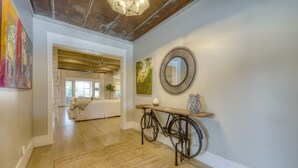 Een hal met een houten vloer, een geweven vloerkleed, een fiets, een ronde spiegel en een schilderij aan de muur.