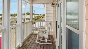 A wooden porch with a rocking chair, white railings, and a view of the surrounding area. - Spacious Beach House • Walk to Beach • Sleeps 12 (Panama City Beach)