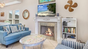 A living room with a blue sofa, a round table, a fireplace, and a bookshelf. - Spacious Beach House • Walk to Beach • Sleeps 12 (Panama City Beach)