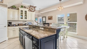 A kitchen with white cabinets, a granite island, and a dining area with a table and chairs. - Spacious Beach House • Walk to Beach • Sleeps 12 (Panama City Beach)