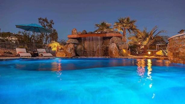 Una piscina con cascada, sillas de descanso y palmeras.