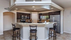 Una cocina moderna con una isla central, armarios de madera oscura, electrodomésticos de acero inoxidable y suelo de baldosas.