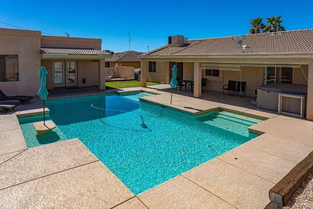 Piscina residencial con agua azul cristalina, rodeada de un patio con sillas y sombrillas.