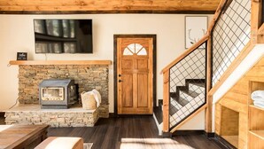 A cozy room with a stone fireplace, a television mounted above it, and a wooden door with a glass panel. - Mountain Escape minutes from Village & Ski Slopes (Big Bear Lake)