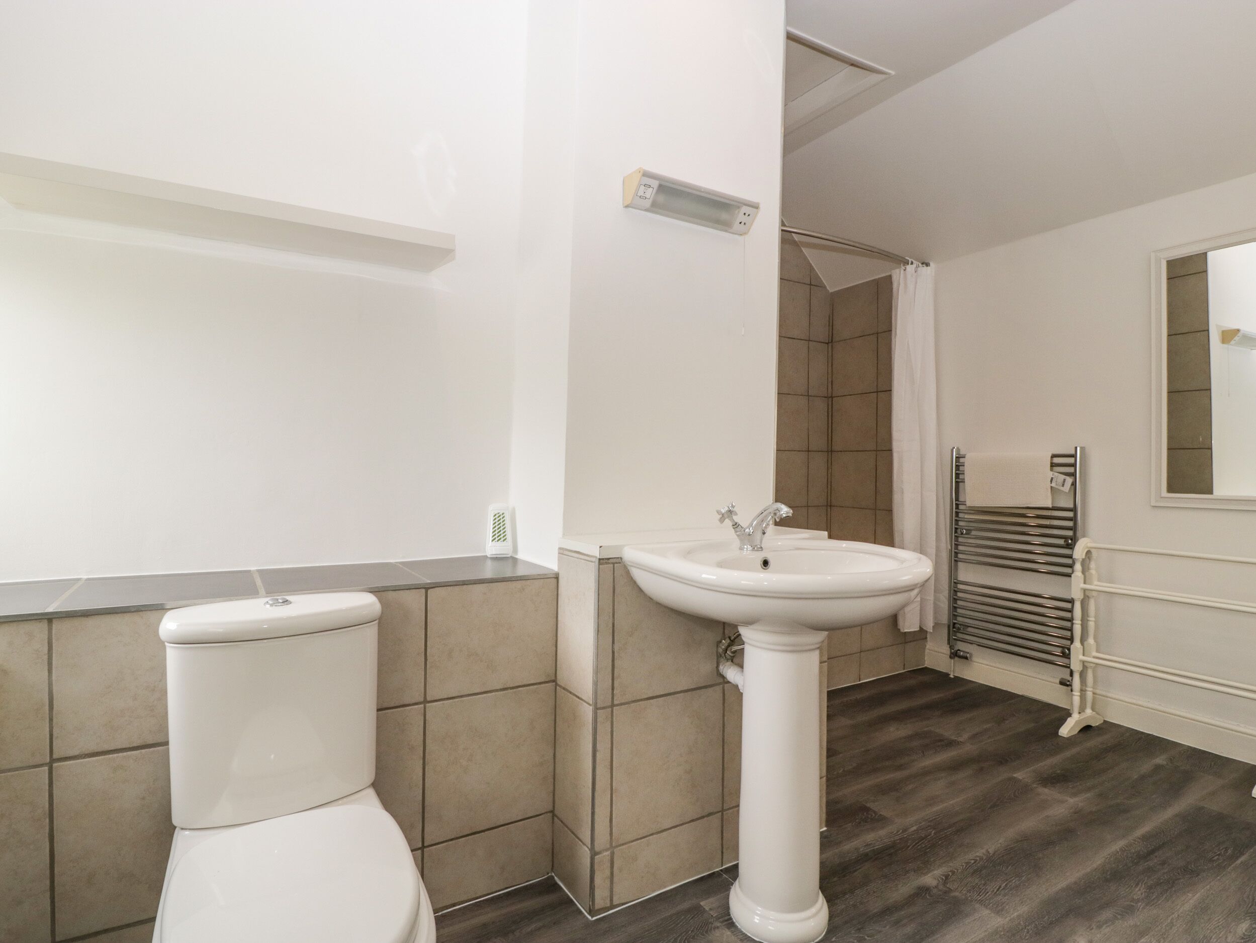 A bathroom with a toilet, a pedestal sink, a towel rack, and a shower area.