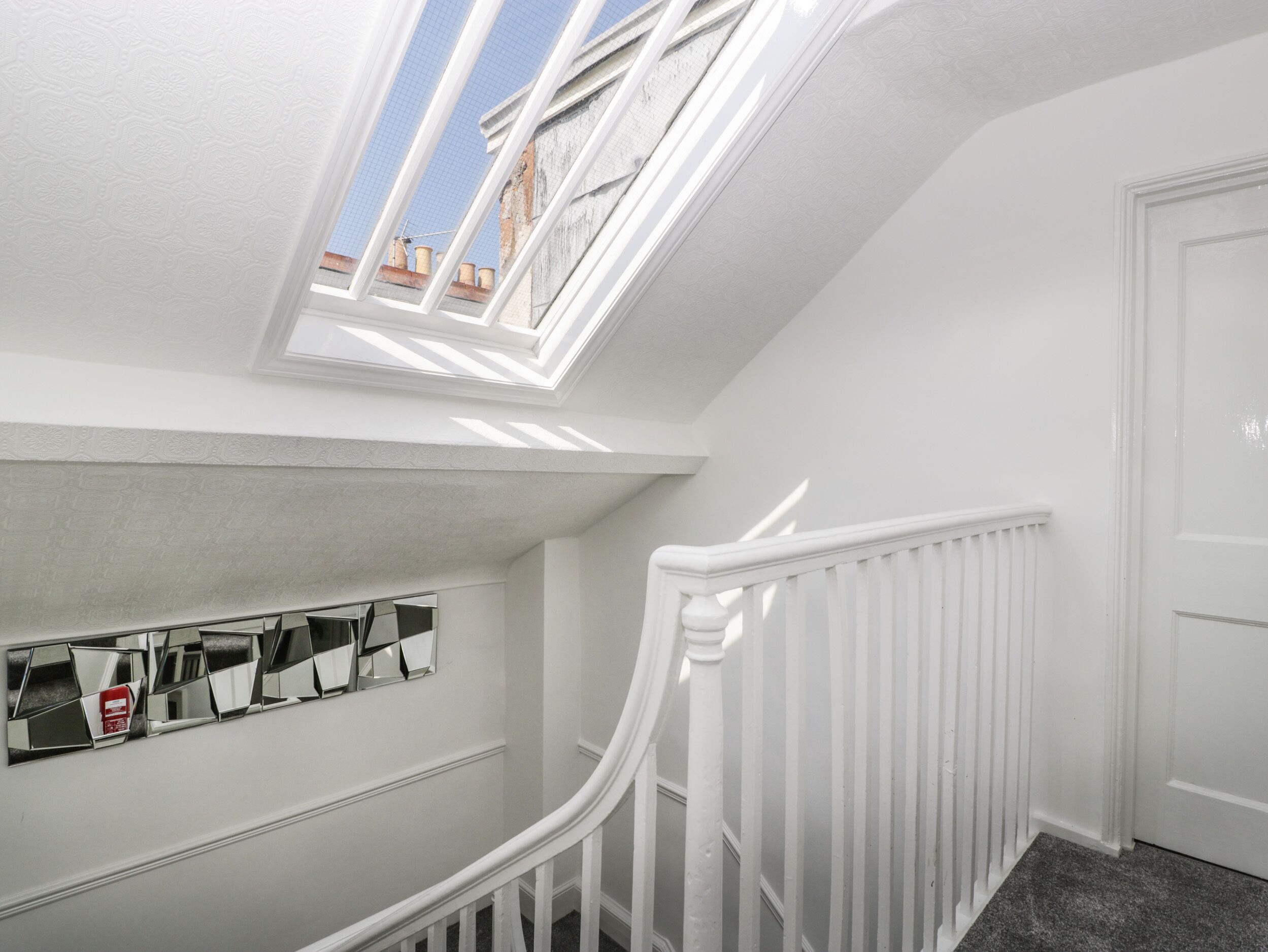 Una escalera blanca con tragaluz y un muro espejado.