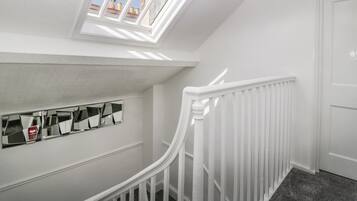 Una escalera blanca con tragaluz y un muro espejado.