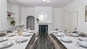 A dining room with a long table set for a meal, a fireplace, and a chandelier.