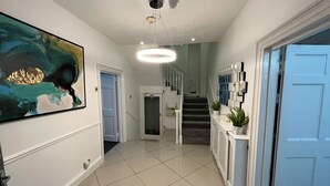 A modern hallway with a staircase, a large abstract painting, and a ceiling light fixture.