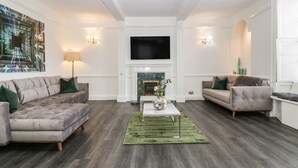 A modern living room with a fireplace, two sofas, a coffee table, and a flat-screen TV.