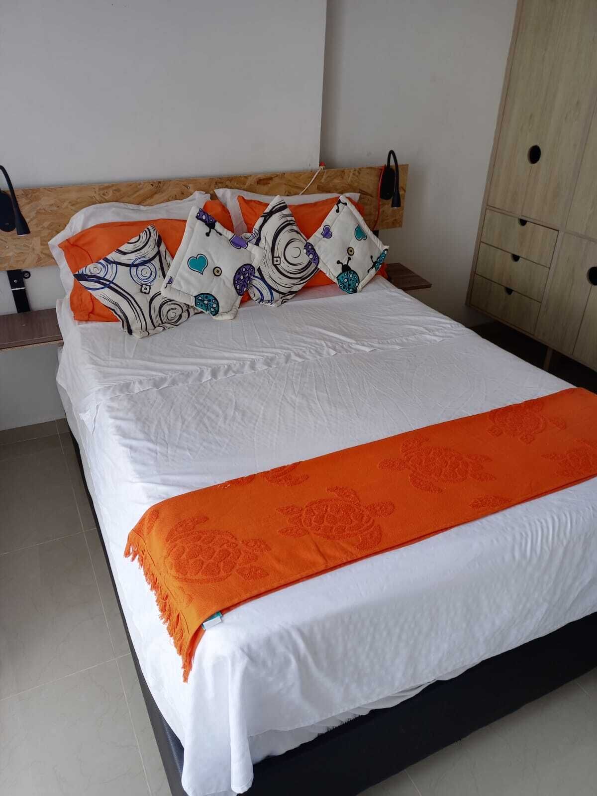 Een bed met witte lakens, oranje kussens en een bijpassend oranje plaid.