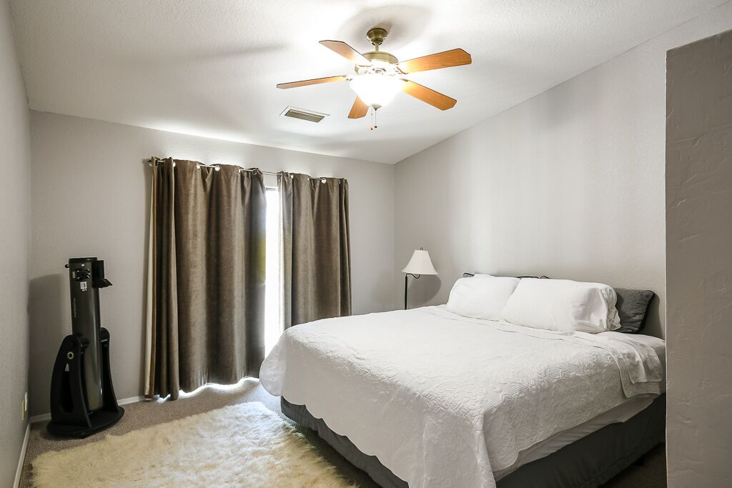 A bedroom with a bed, a ceiling fan, a lamp, and a guitar.