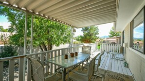 Eine überdachte Terrasse mit Tisch und Stühlen, ein weißer Zaun und Blick auf Bäume und Gebäude.