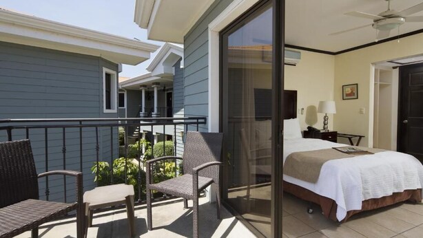 Een balkon met rieten stoelen, een bed met een witte sprei en een plafondventilator.