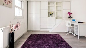 Quarto moderno e bem iluminado, com um guarda-roupa grande, uma escrivaninha e uma cadeira, e um tapete roxo.