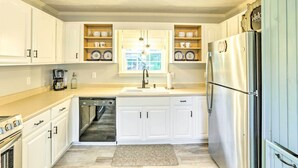 A kitchen with white cabinets, a stainless steel refrigerator, a dishwasher, and a window with a view. - Waterfront Home: Spectacular On-Site Fishing! (Panacea)