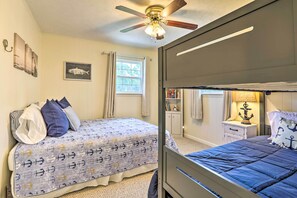 Une chambre avec un lit superposé, un ventilateur de plafond, une fenêtre avec des rideaux, une table de chevet avec une lampe et une bibliothèque.