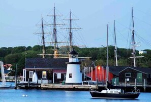Un puerto con un faro, un muelle con un velero, y un edificio con techo rojo.