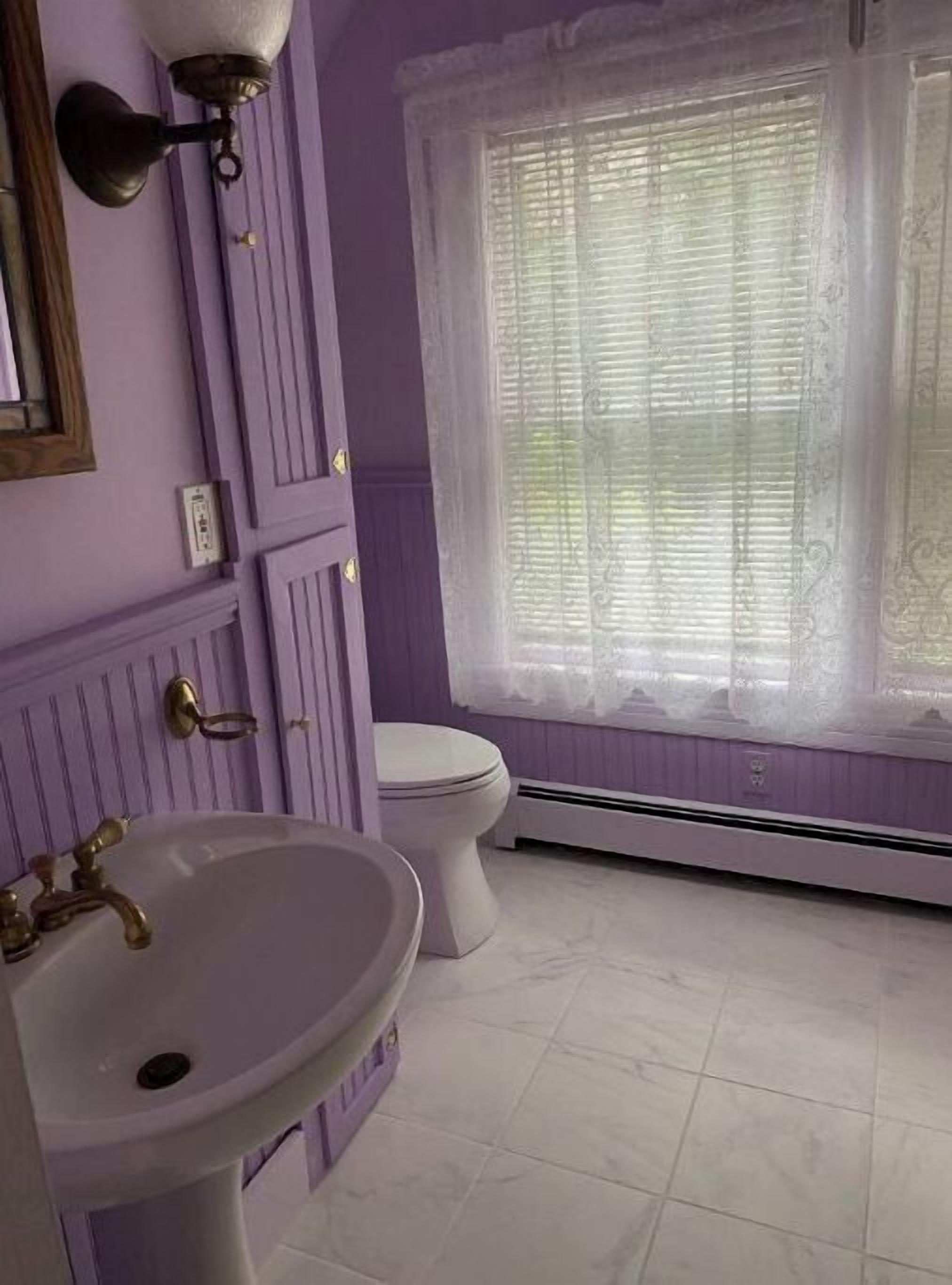 Ein Badezimmer mit einem weißen Waschbecken, einer Toilette und einem Fenster mit Spitzenvorhängen.