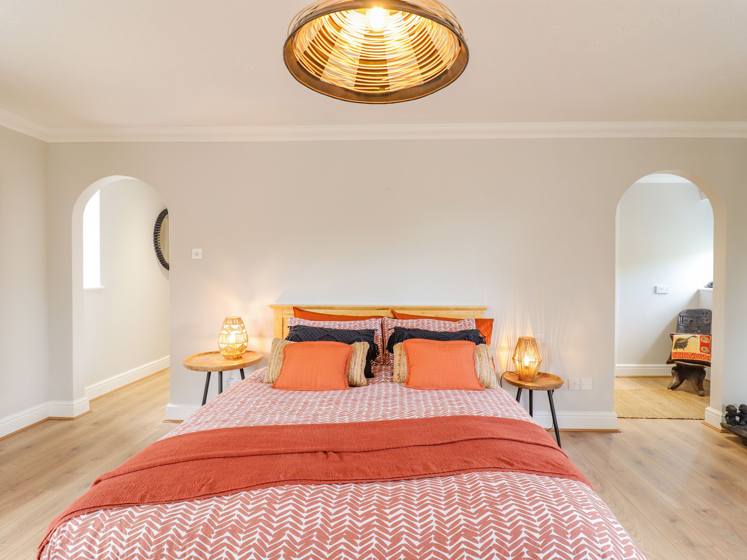A bedroom with a wooden bed, orange bedding, two bedside lamps, and a unique circular ceiling light.