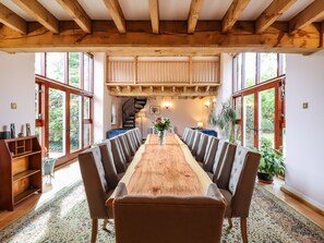 A dining area with a long wooden table, upholstered chairs, and a spiral staircase in the background. - Yew Tree Farm (Aylesbury)
