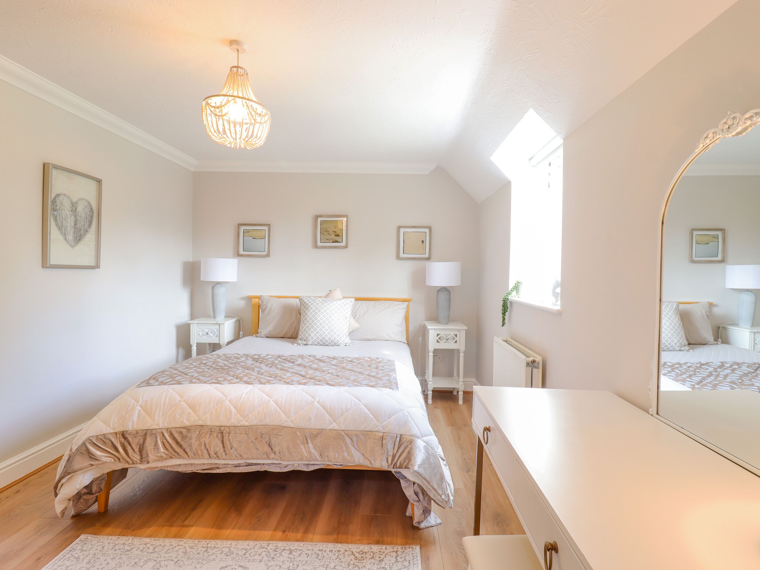 A bedroom with a large bed, bedside tables, a dresser, a mirror, and a chandelier.