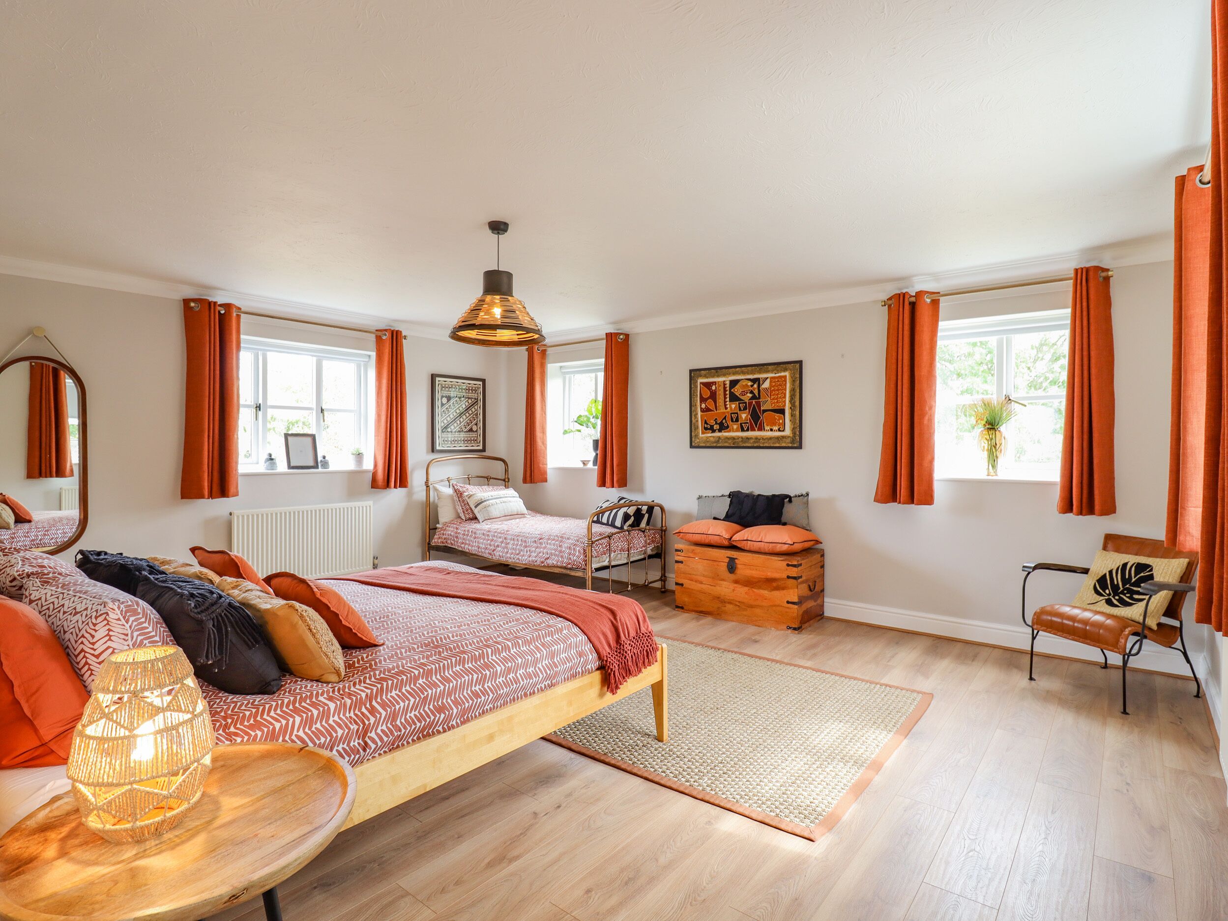 A bedroom with two beds, a wooden chest, a chair, and a hanging light fixture.