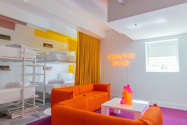 A modern hotel room with bunk beds, a bright orange sofa, a white coffee table, and a neon sign. - The Gallatin (Queen Suite 111) 4 Full Beds (Nashville)