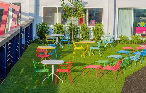 An outdoor seating area with multiple tables and chairs, surrounded by a well-maintained lawn and a building with large windows. - The Gallatin (Queen Suite 111) 2 Queen Beds (Nashville)