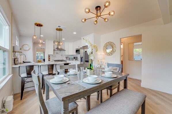 A modern kitchen with white cabinets, a central island, and a dining area with a wooden table set for four. - Exquisite Luxury Living In 3BR 2BA North Park Home (San Diego)