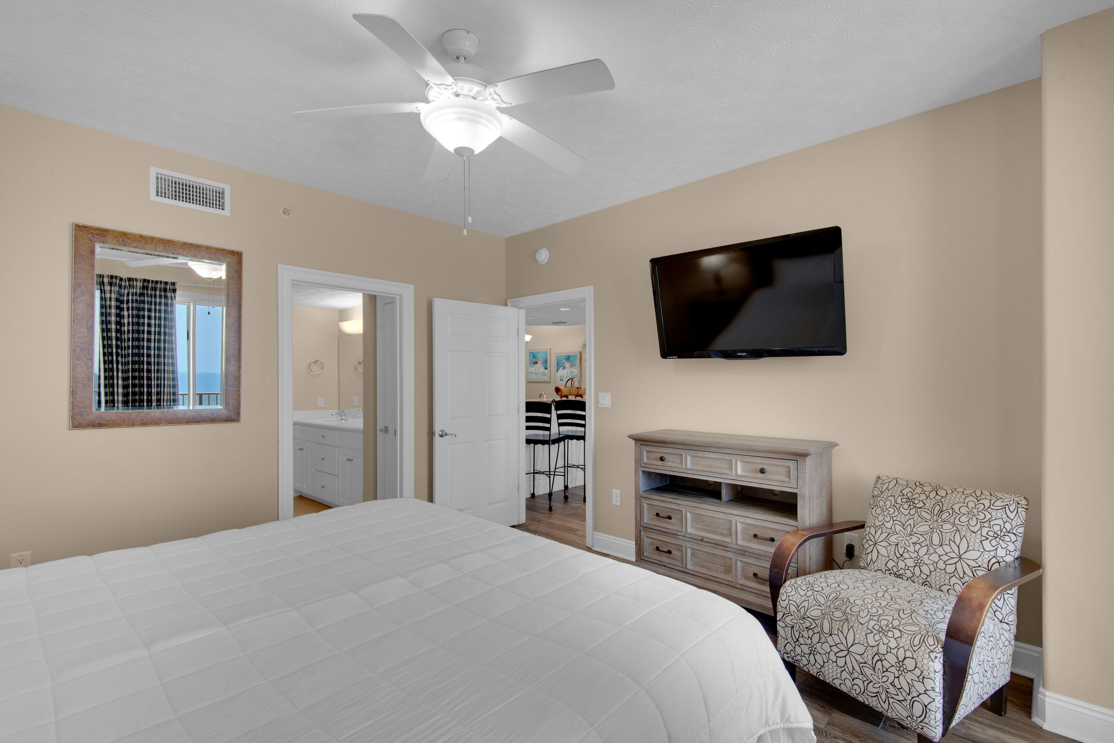 A bedroom with a large bed, a ceiling fan, a TV mounted on the wall, and a chair.