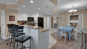A spacious kitchen with white cabinets, a central island, and a dining area with a blue table and white chairs. - Treasure Island 0809 (Panama City Beach)