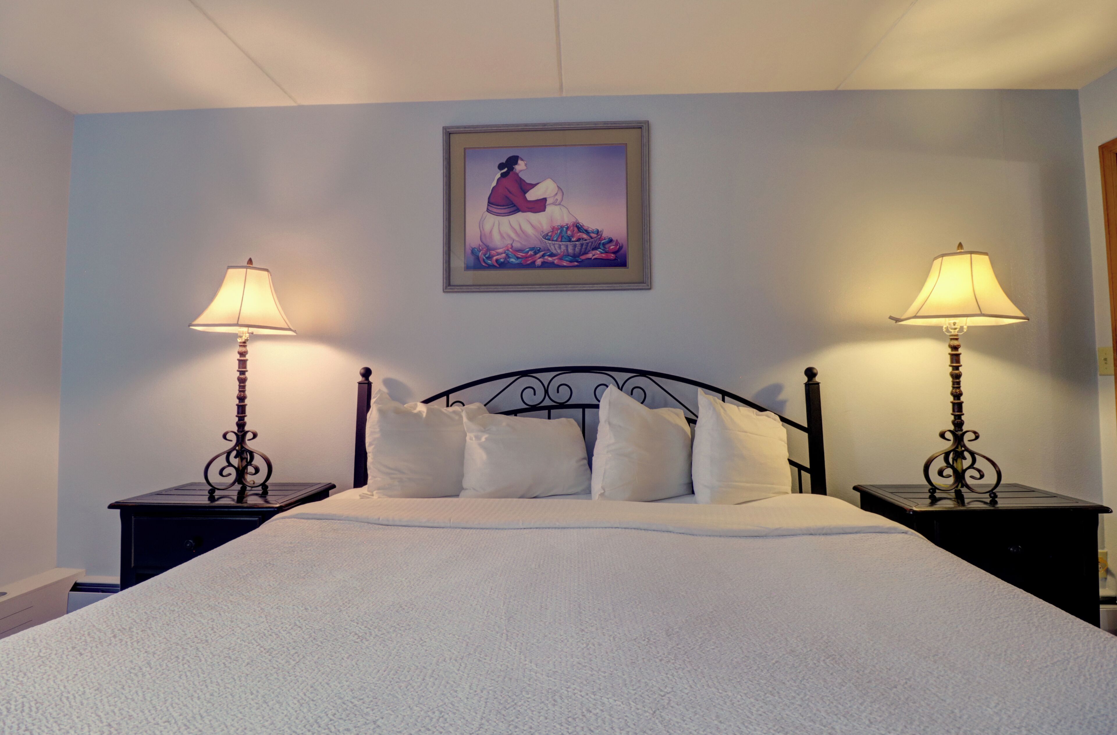 A neatly made bed with white linens, two bedside tables with lamps, and a framed picture on the wall.