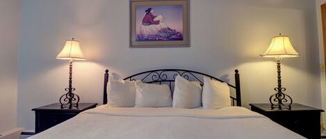A neatly made bed with white linens, two bedside tables with lamps, and a framed picture on the wall.