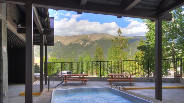 A covered outdoor area with a hot tub, picnic tables, and a view of mountains. - Perfect Ski-In/Ski-Out Hotel Room, Steps to American E Chairlifts, Hot Tub (Copper Mountain)