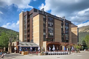 Een meerlaags hotel met terras en een berg op de achtergrond.