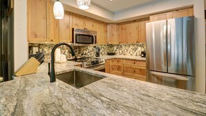 Eine Küche mit Granit-Arbeitsplatten, Holzschränken, Edelstahlgeräten und Pendelleuchten.