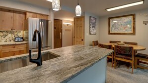 Eine Küche mit Granit Arbeitsplatte, Edelstahlgeräten, Holzschränken und Pendelleuchten.