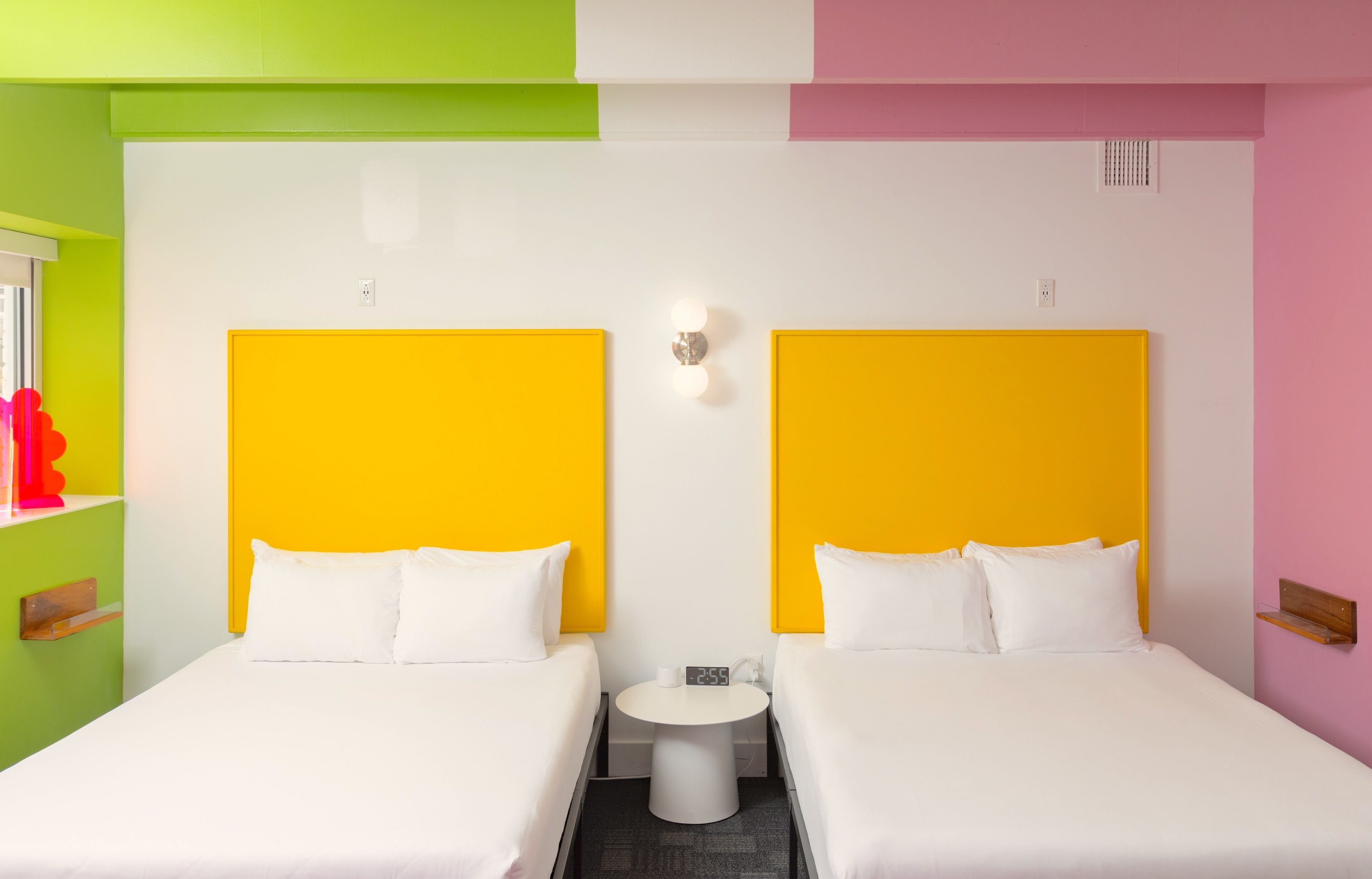 A hotel room with two beds, a small round table, and a wall clock.