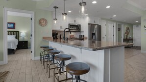 A modern kitchen with a central island, bar stools, stainless steel appliances, and pendant lighting. - Treasure Island 0903 (Panama City Beach)