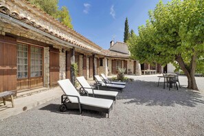 A building with stone walls, a tiled roof, and a gravel courtyard with sun loungers and a table.