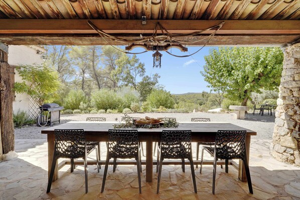 Un patio al aire libre con piso de piedra, una mesa de madera y sillas de metal.
